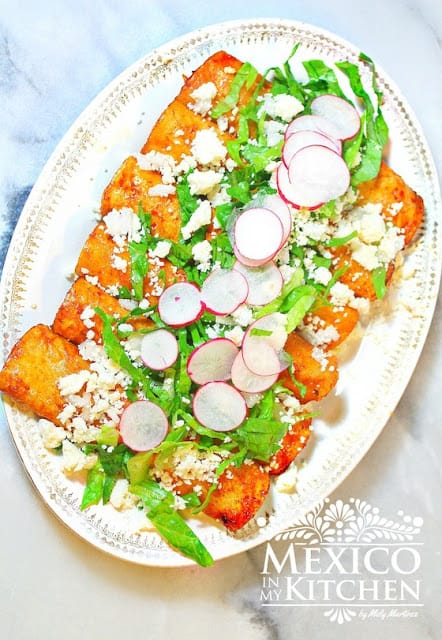 Red enchiladas served on a platter and topped off with cotija cheese and sliced radishes 