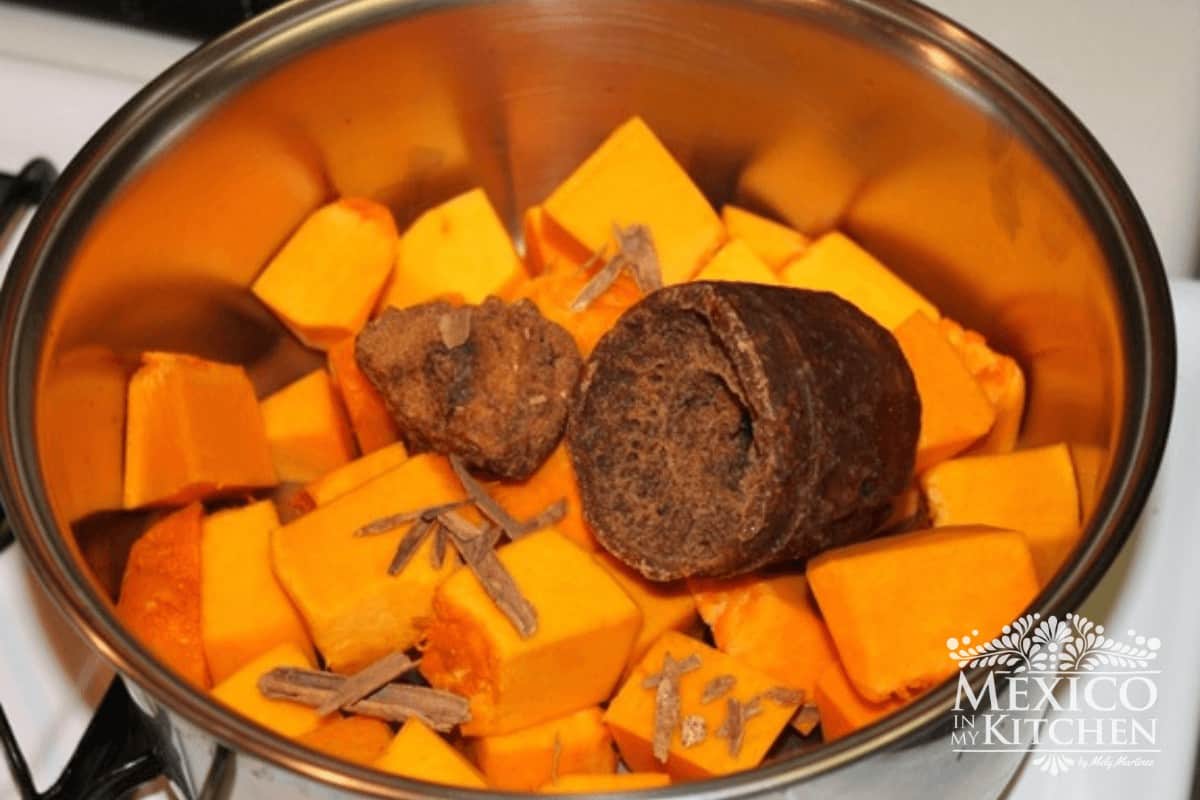 Cubes of pumpkin with piloncillo and spices placed in a pot.