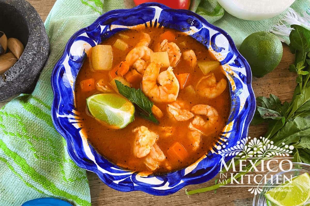 Shrimp soup served in a bowl garnished with lime and epazote.