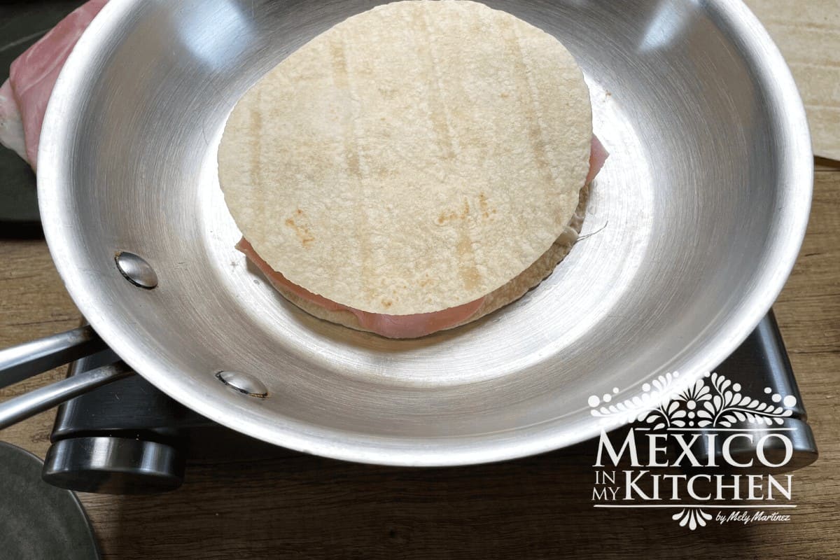 Flour tortilla in a frying pan filled with cheese.