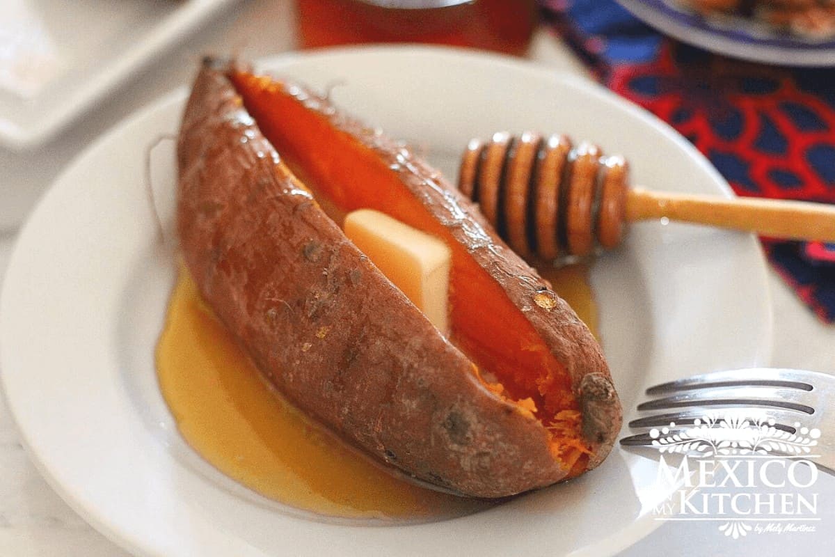 Baked sweet potato with butter and honey on a plate.