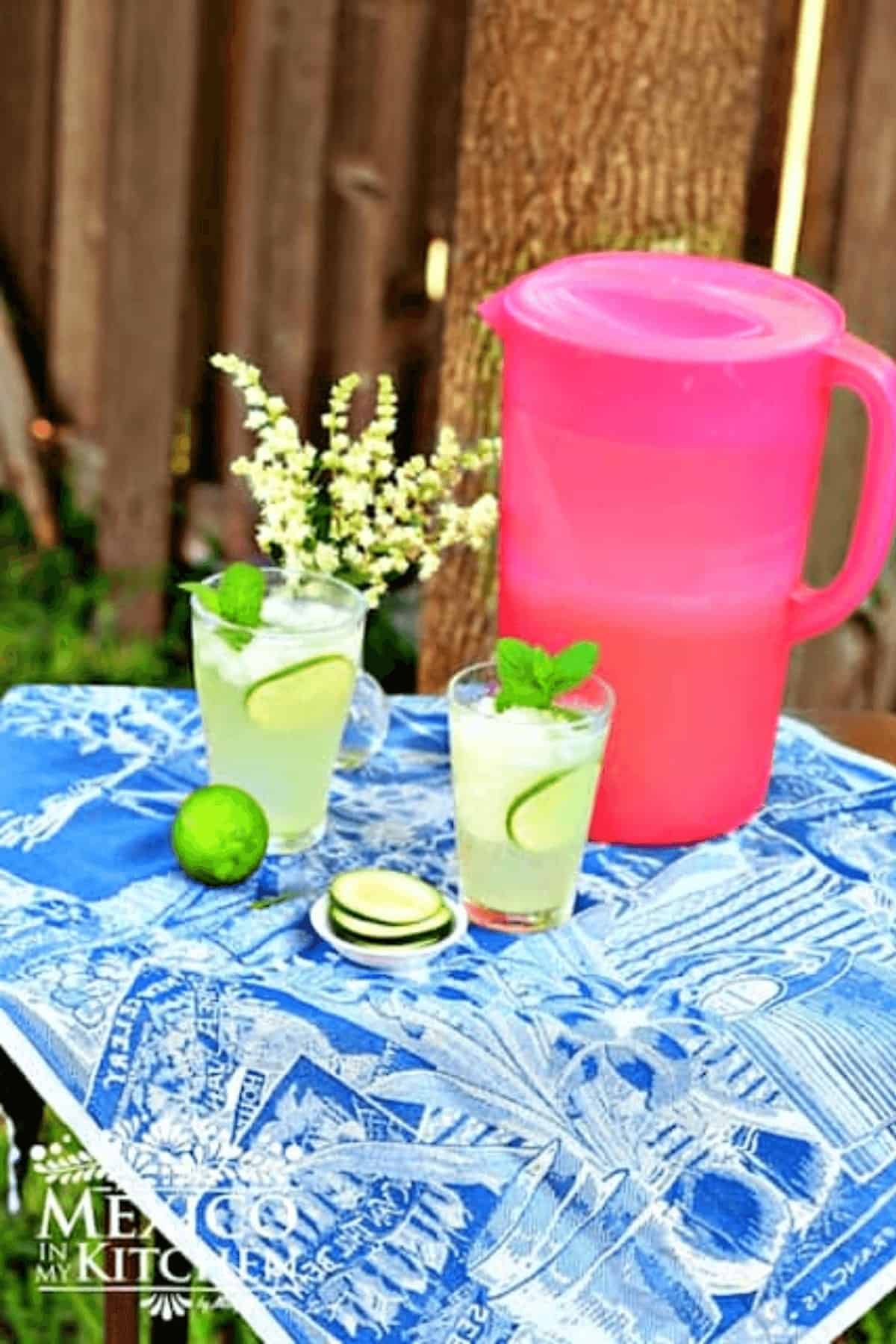 A pitcher and two cups with cucumber lime agua fresca.