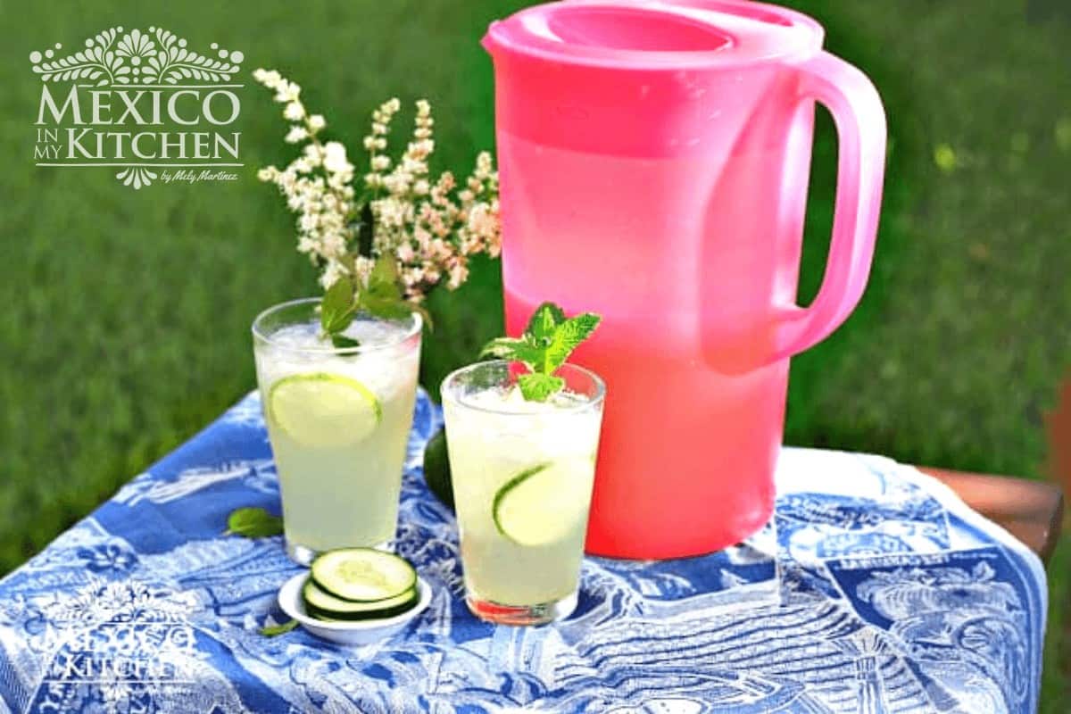 A pitcher and two cups with cucumber lime agua fresca.