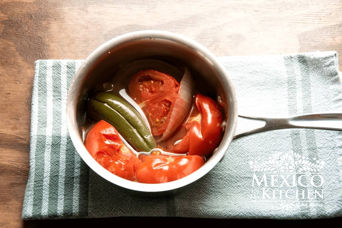 Cooked Tomatoes, jalapeños, slice of onion, with water in a saucepan.