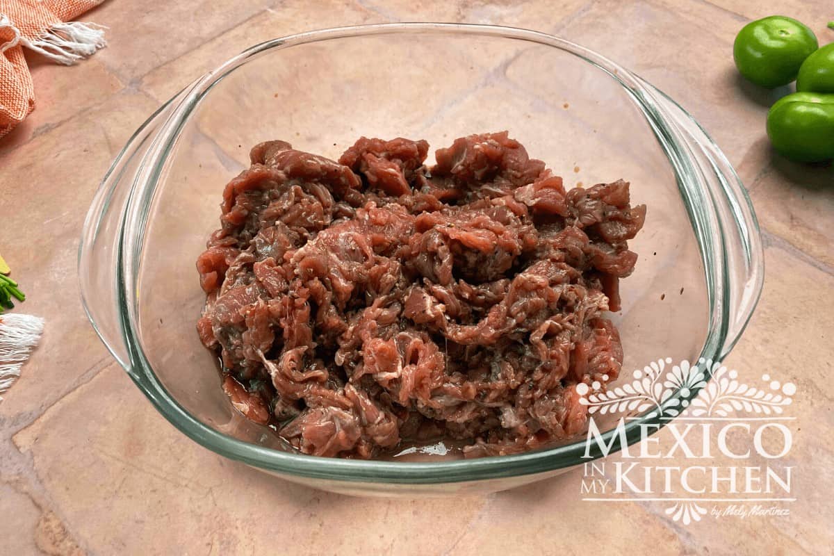 Marinated pieces on beef in a glass bowl.