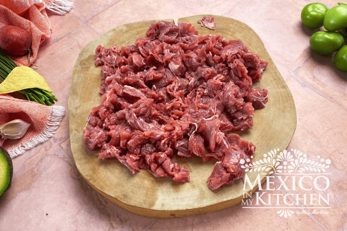 Beef chopped in small pieces over a cutting board.