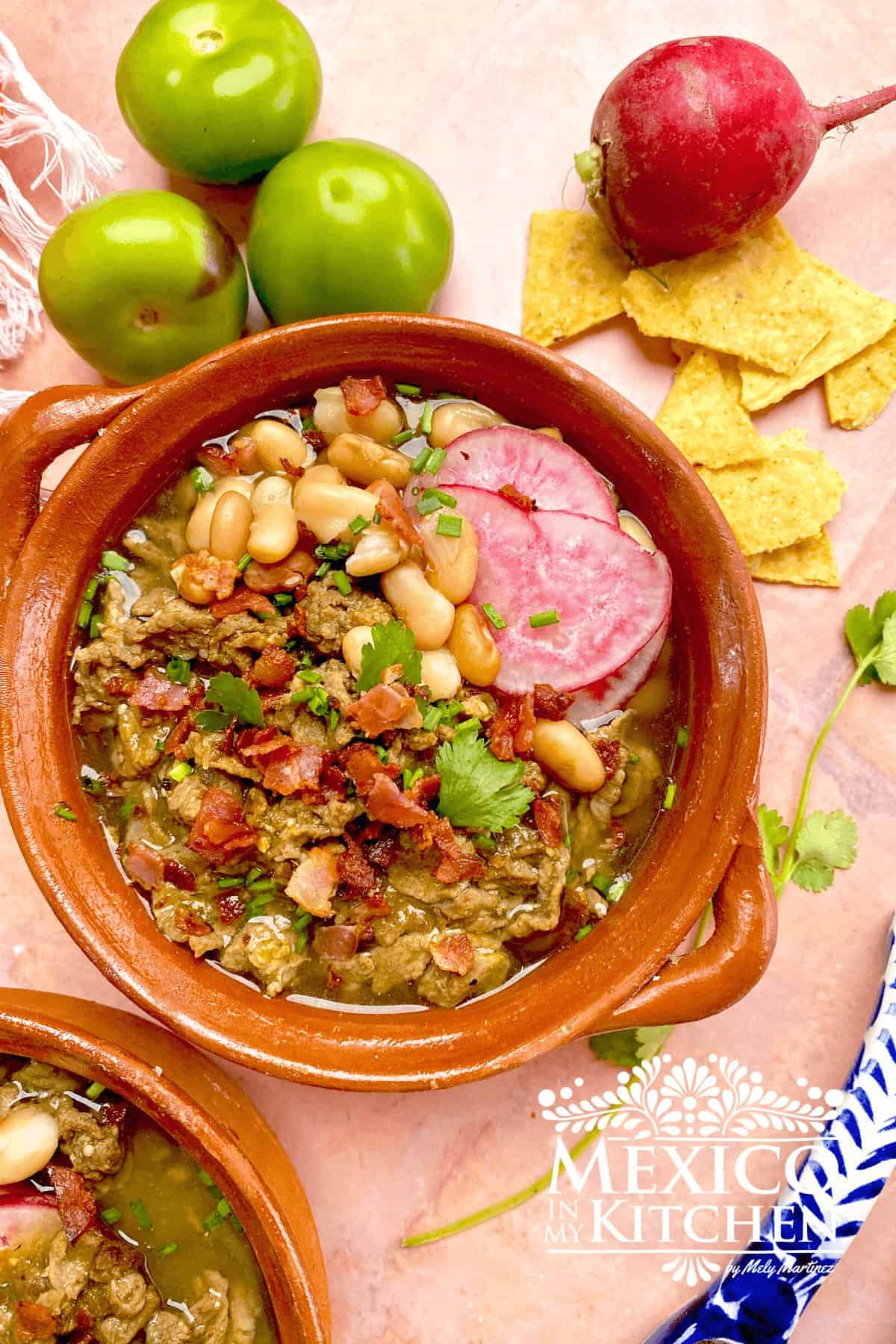 Carne en su jugo served in a bowl topped with beans, radishes, and bacon.