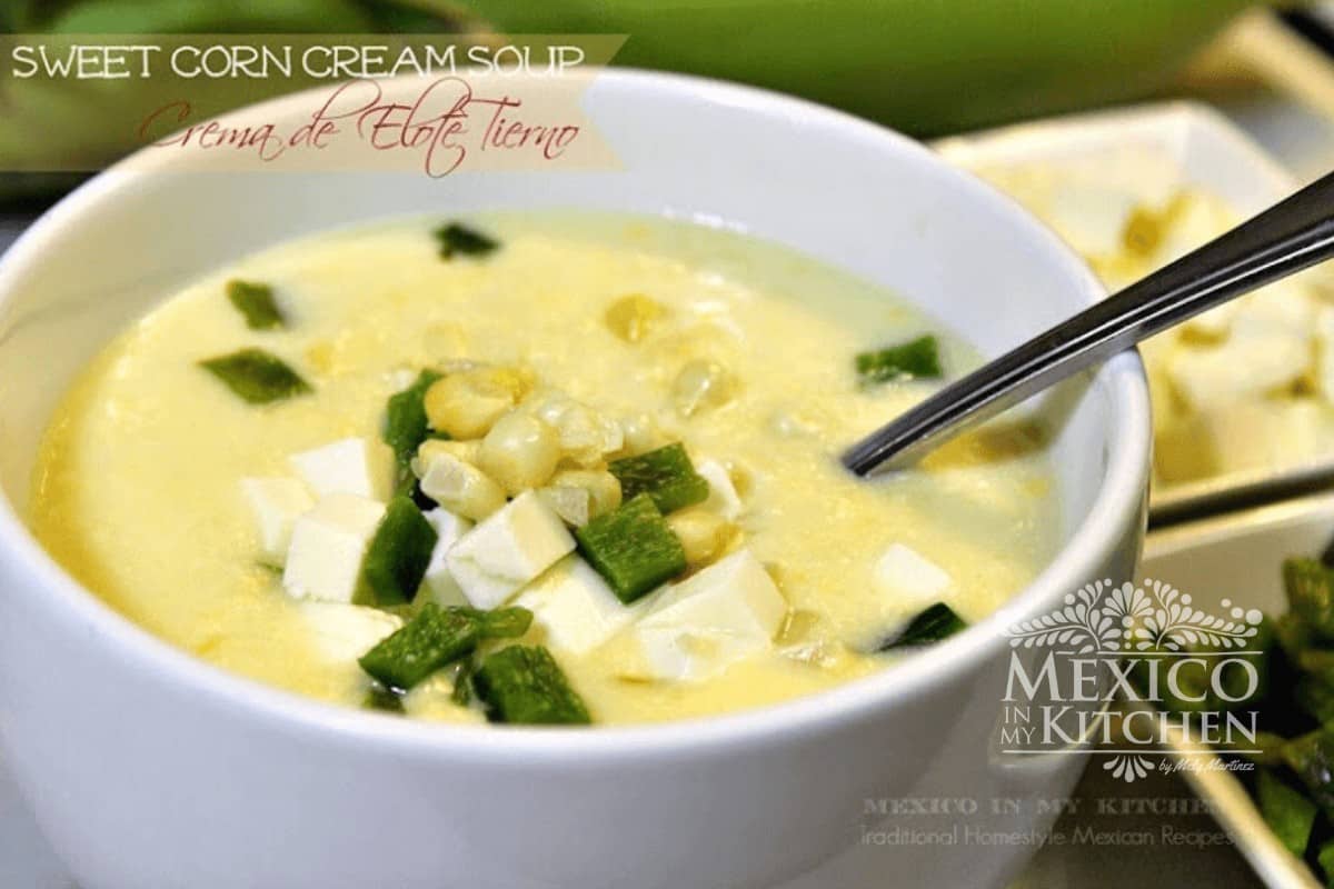 Corn soup served in a white bowl and topped with corn, poblano peppers strips, and panela cheese.