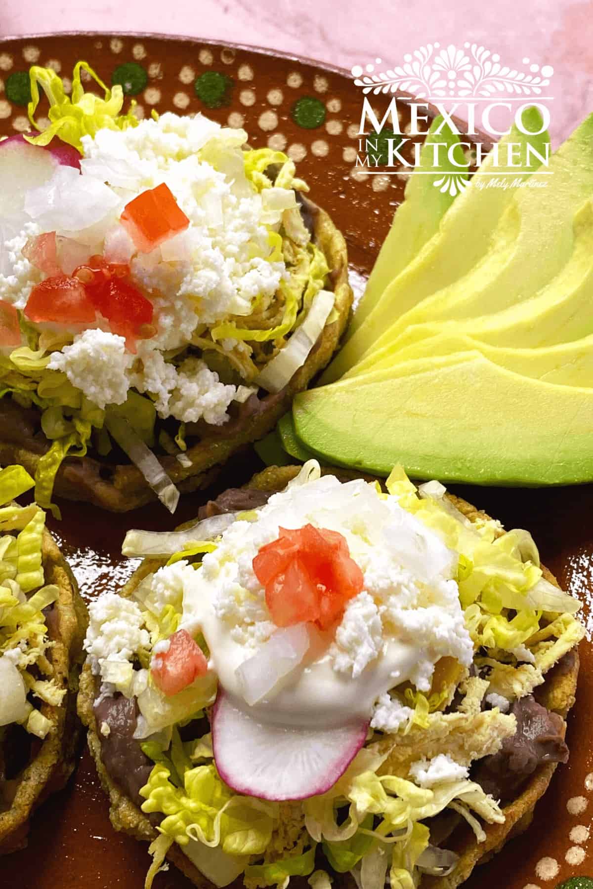 Close up of Mexican sopes, topped with lettuce, Mexican crema, tomatoes, and queso fresco.