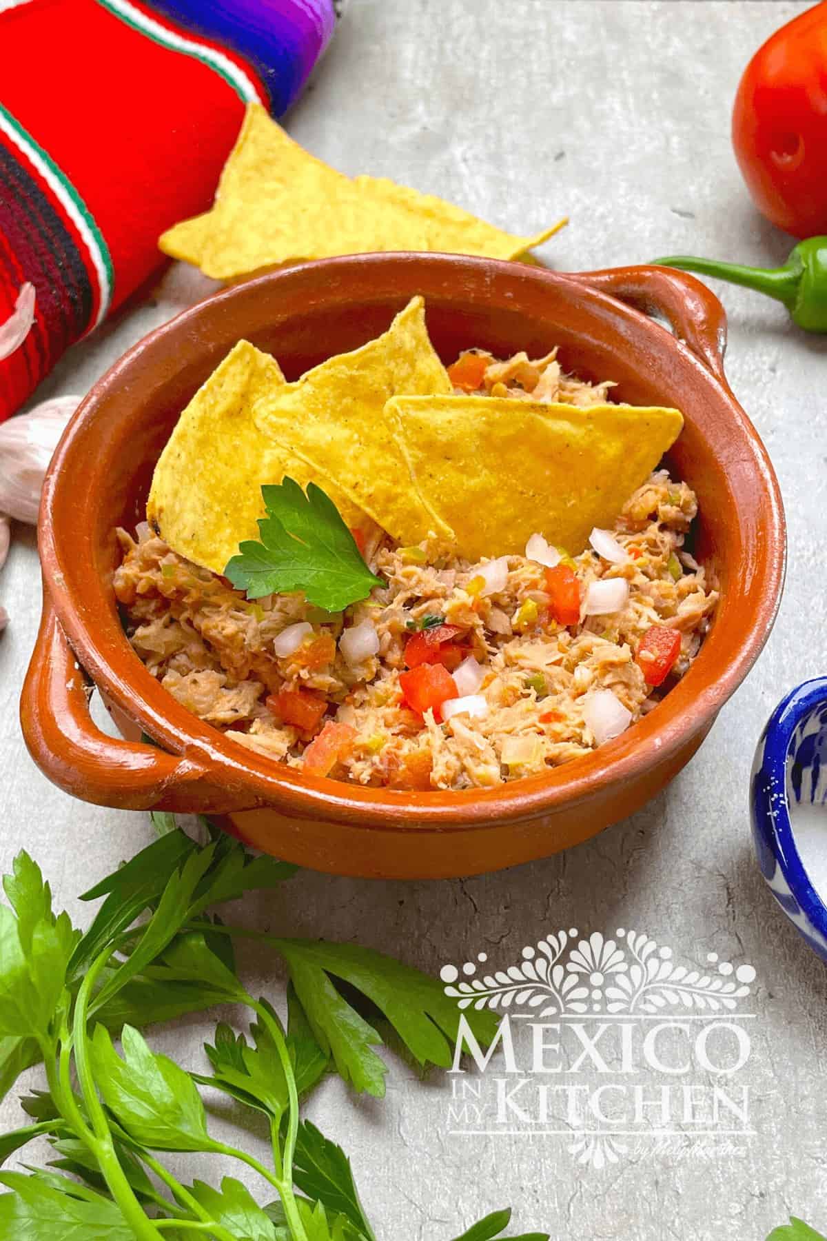Mexican Tuna Salad serve in a clay pot and topped with parsley and tortilla chips.