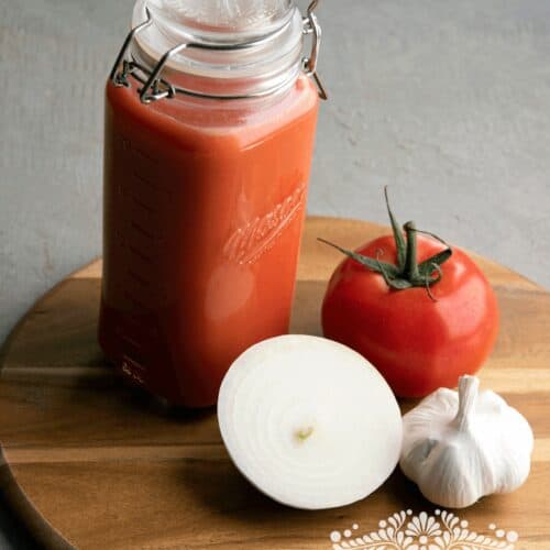 Jar with tomato sauce next to tomatoes, onions and garlic.