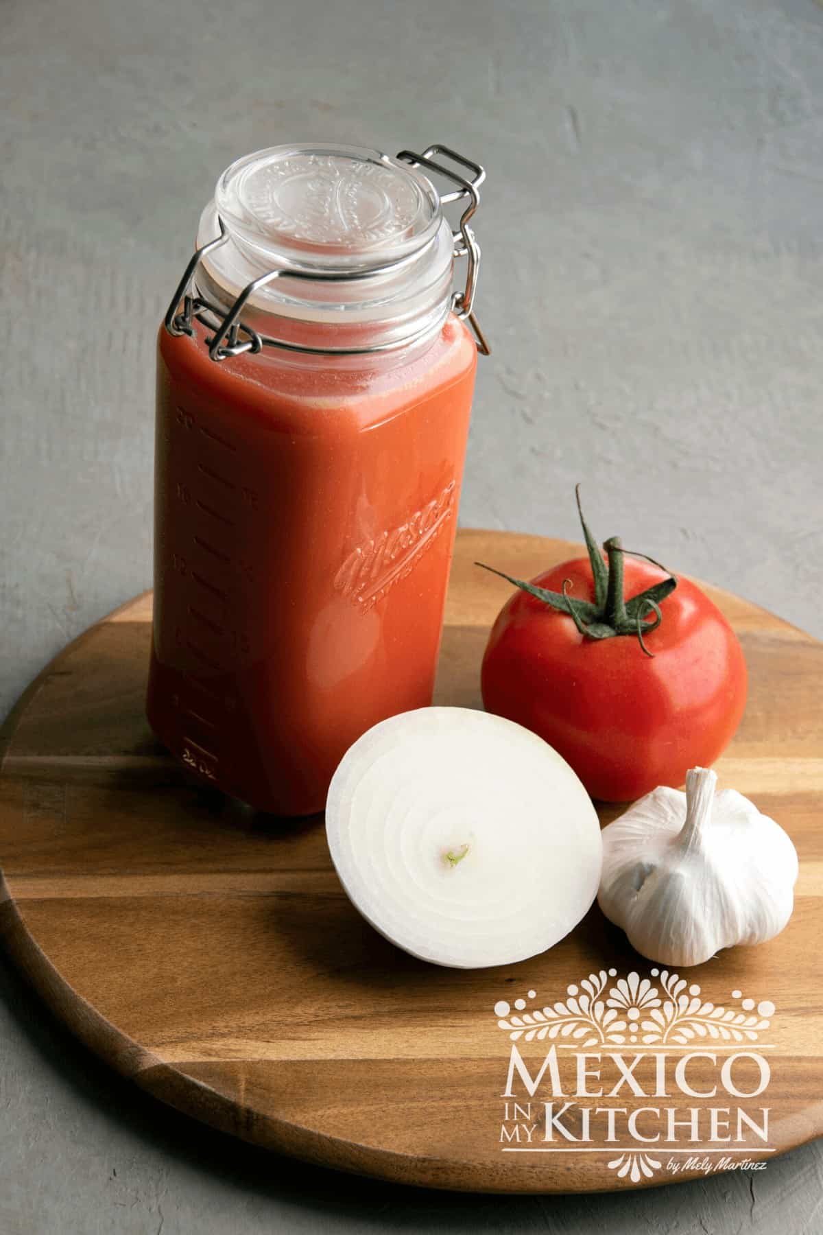 Jar with tomato sauce next to tomatoes, onions and garlic.