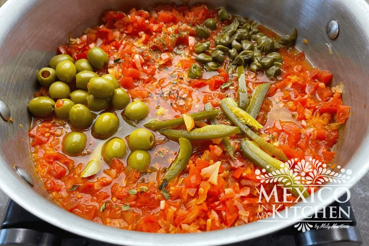 Tomato mixture topped with peppers, olives and capers in a cooking pot.