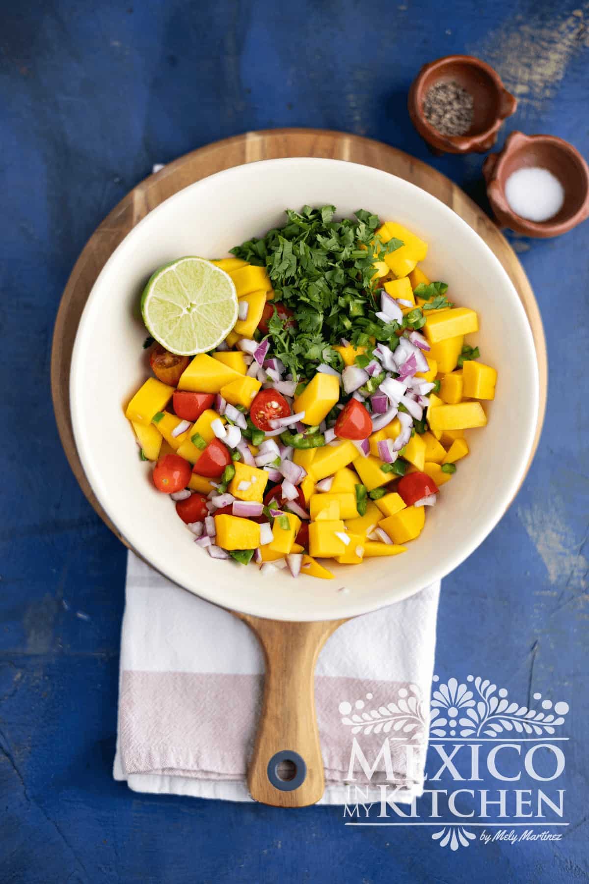 Chopped mango chunks, tomatoes, red onions, jalapeños, and cilantro served in a bowl.