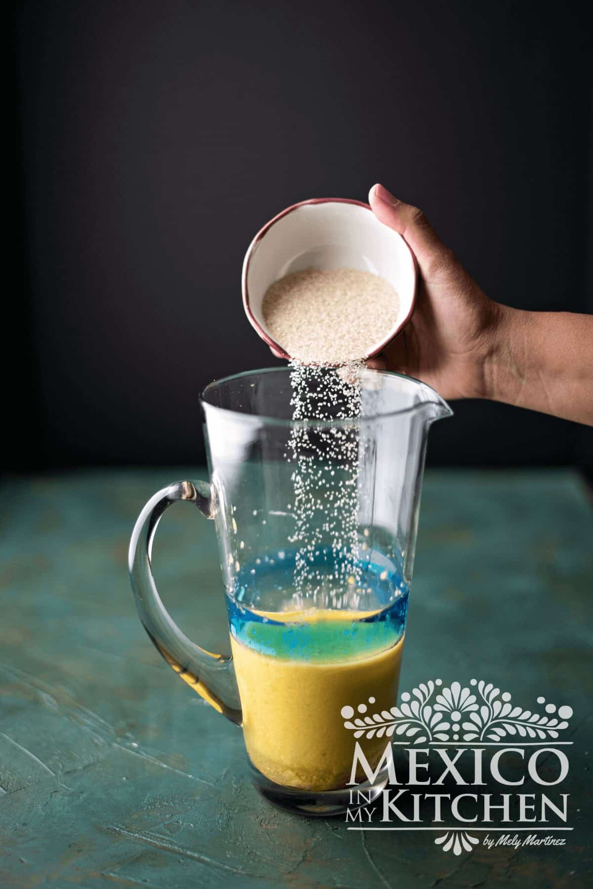 Sugar is added to a glass pitcher of fruit puree.