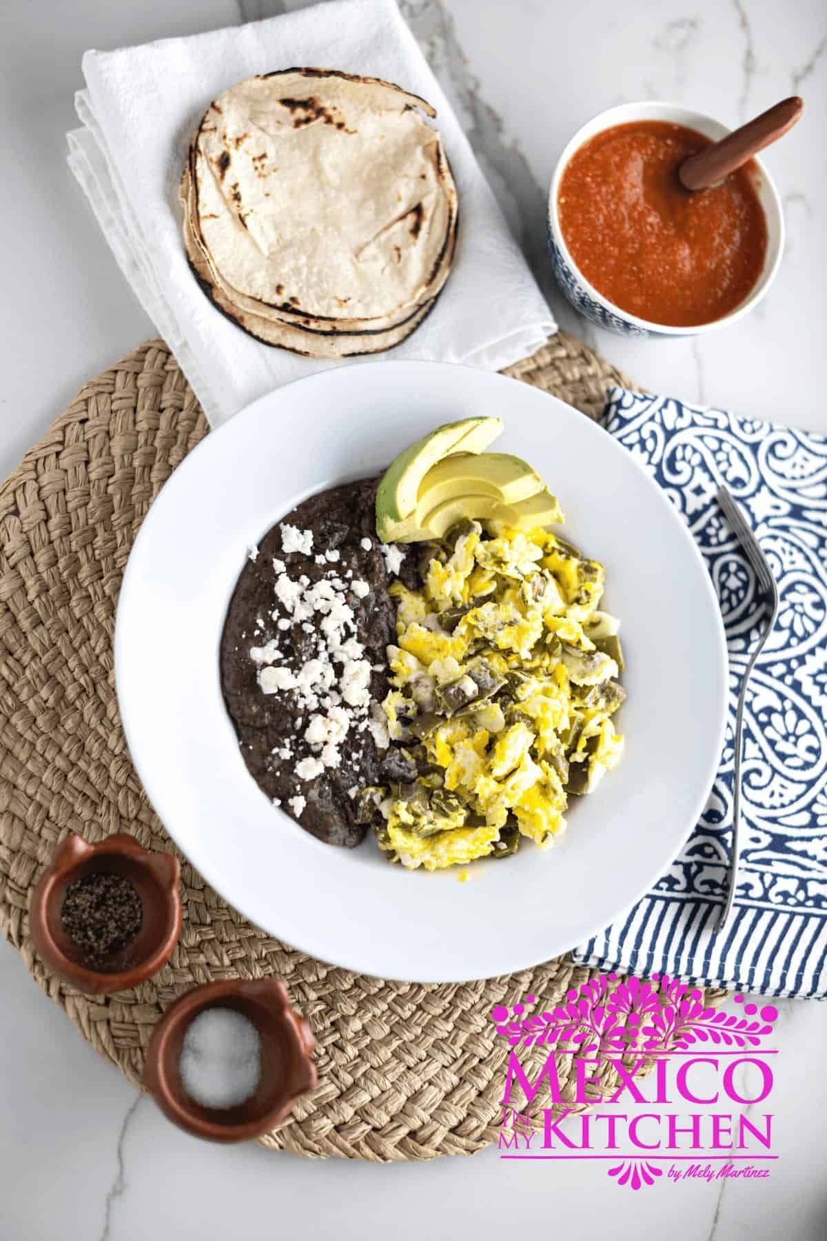 Serving of nopales con huevos next to black beans in a white plate.