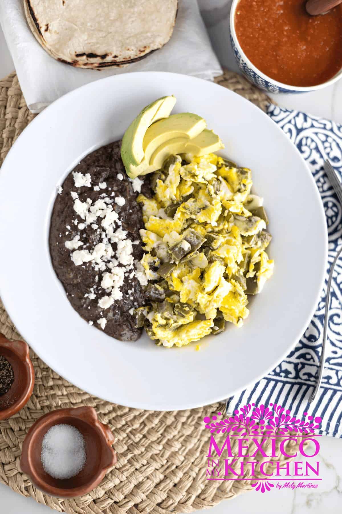 Serving of nopales con huevos next to black beans in a white plate.