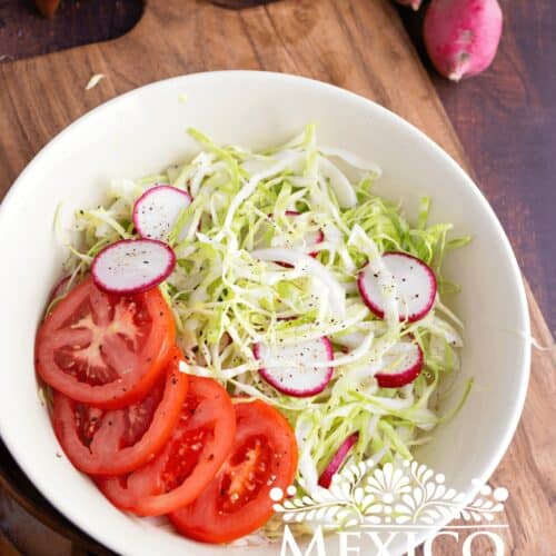 Mexican coleslaw made with shredded cabbage with sliced radishes, onion, and tomato in a salad bowl.