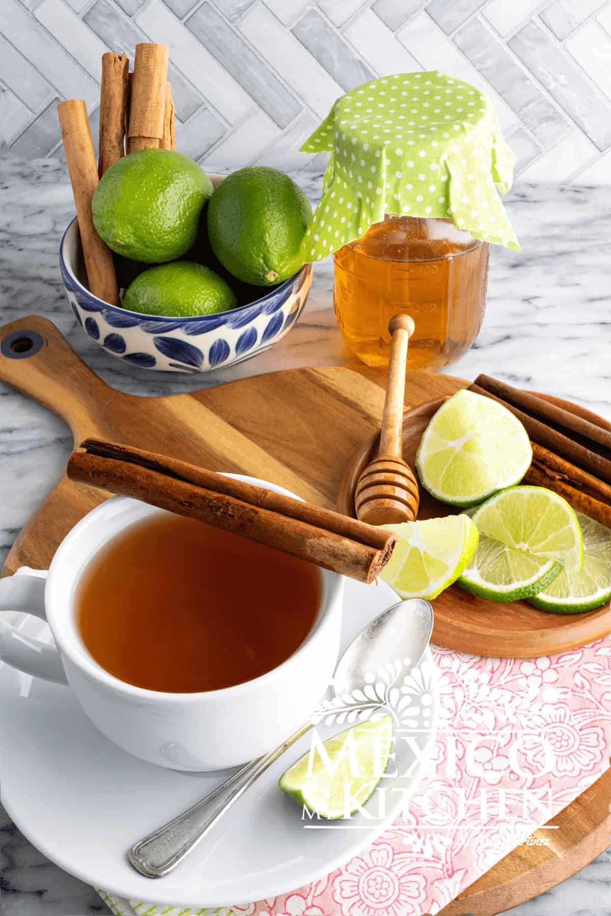 Cinnamon honey tea served in a white cup, next to lime wedges and cinnamon sticks.