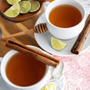 Cinnamon honey tea served in white cups, next to lime wedges and cinnamon sticks.