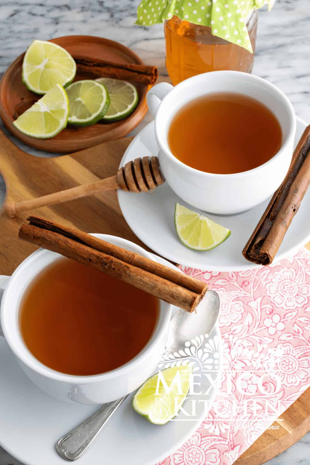 Cinnamon honey tea served in white cups, next to lime wedges and cinnamon sticks.