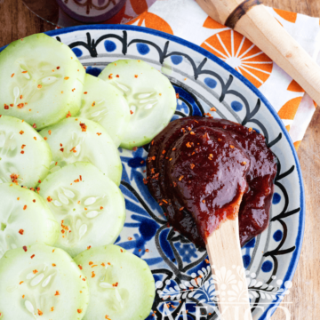 Slices of cucumber next to a spoon full of chamoy sauce.