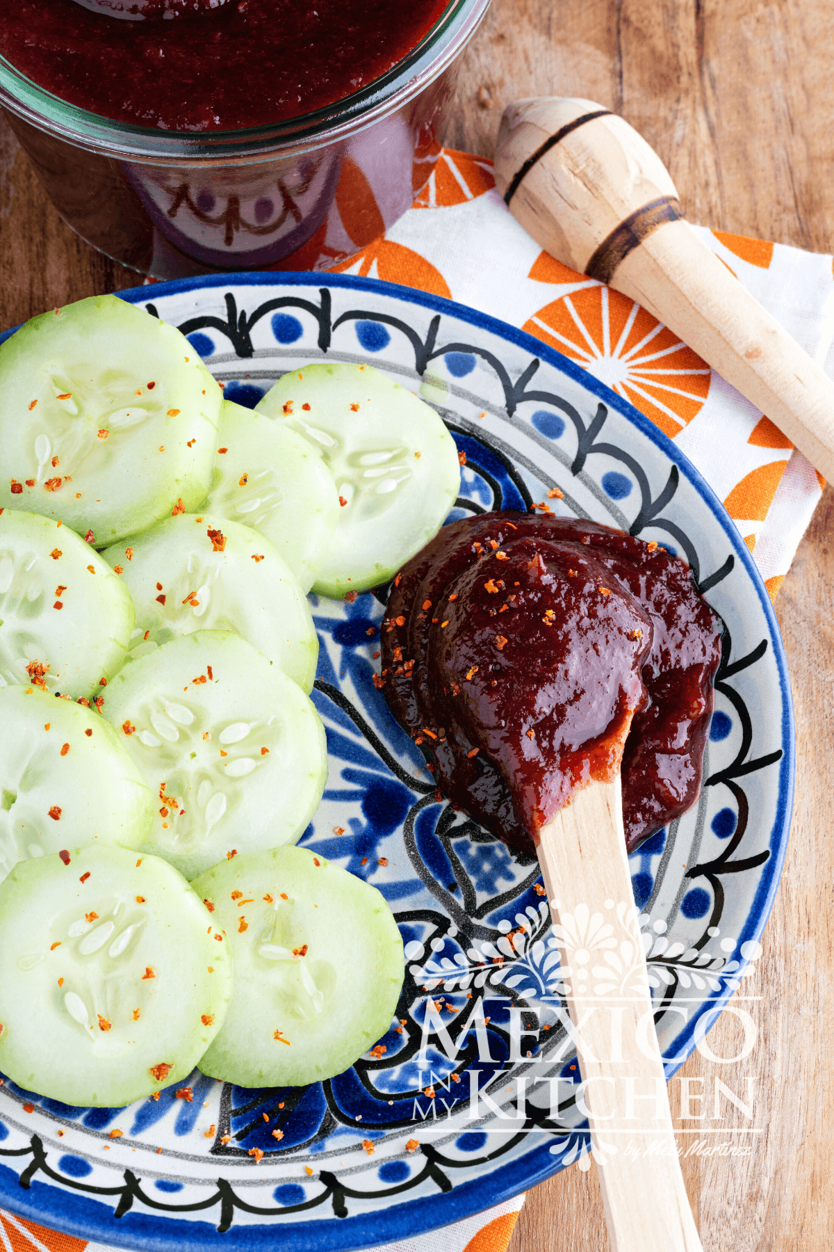 Slices of cucumber next to a spoon full of chamoy sauce.