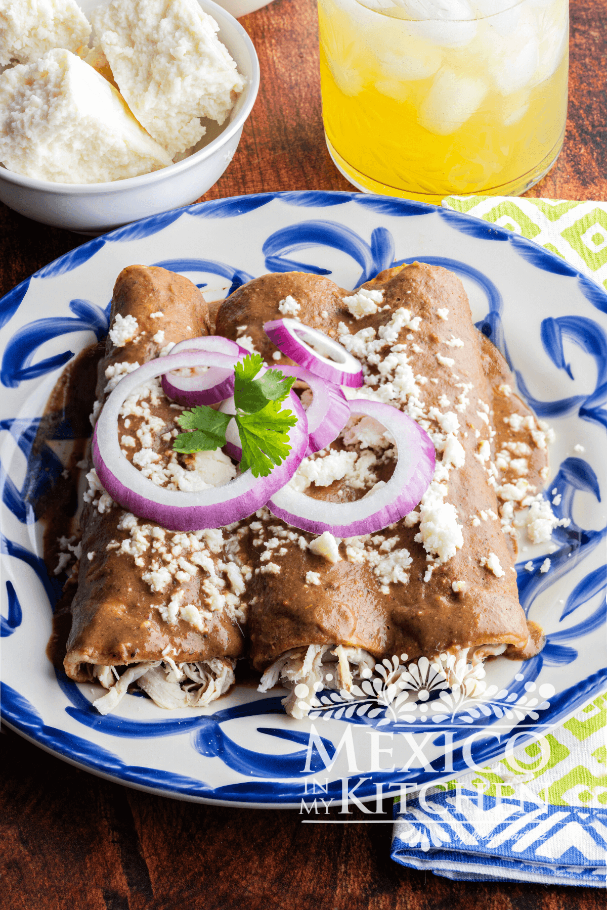 Enfrijoladas served in a plate topped with queso fresco and slices of purple onion.