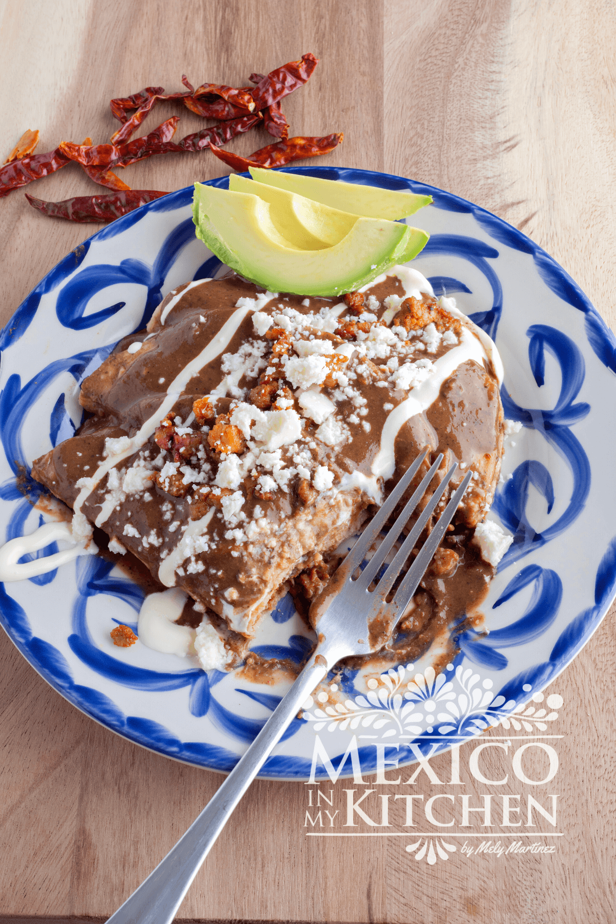 Enfrijoladas served in a plate, topped with Mexican crema, queso fresco and avocado slices.