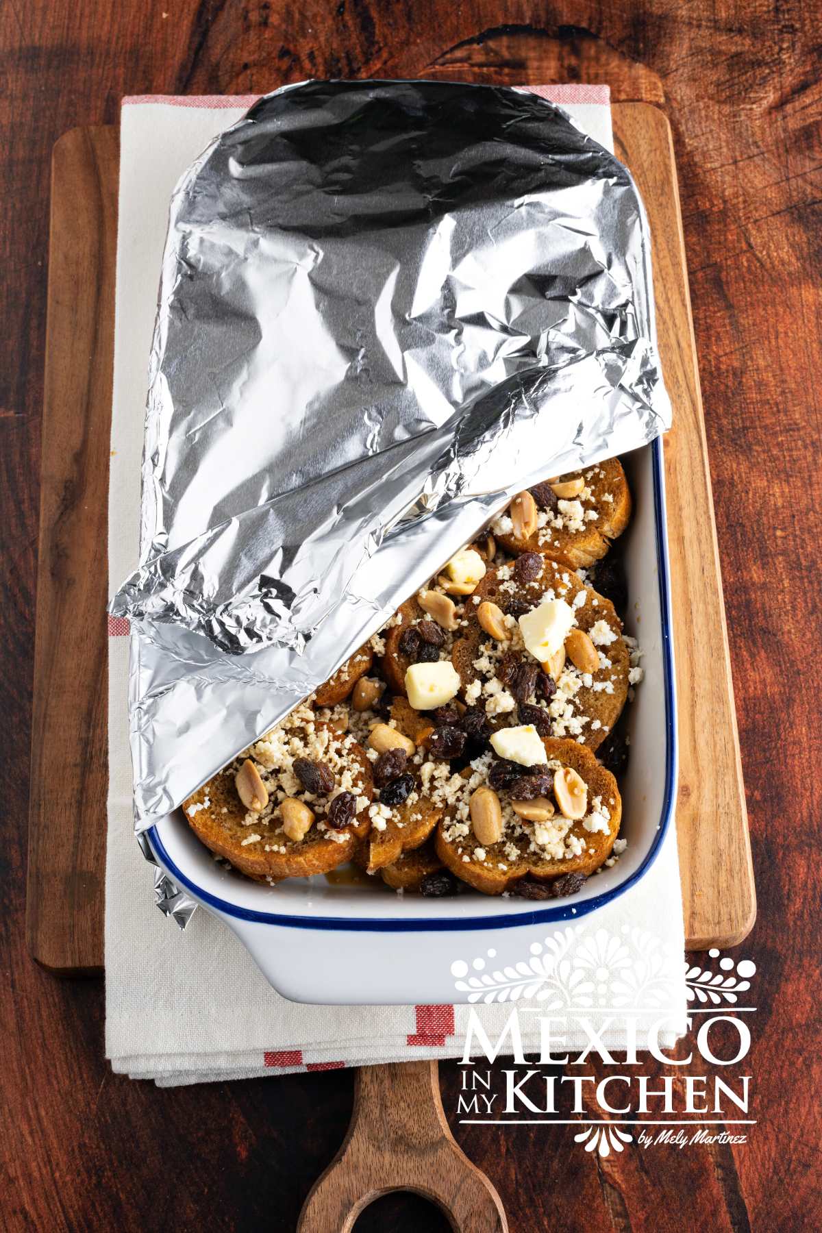 Toasted slices of bread topped with piloncillo cinnamon syrup, cheese, peanuts, and raisins, covered with aluminum foil.