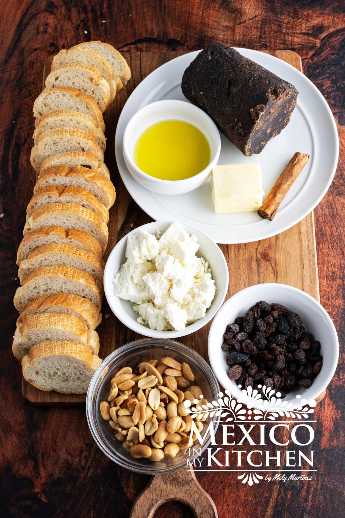 Slices of bread, cotija cheese, nuts, raisins, piloncillo and Mexican cinnamon on a cutting board.