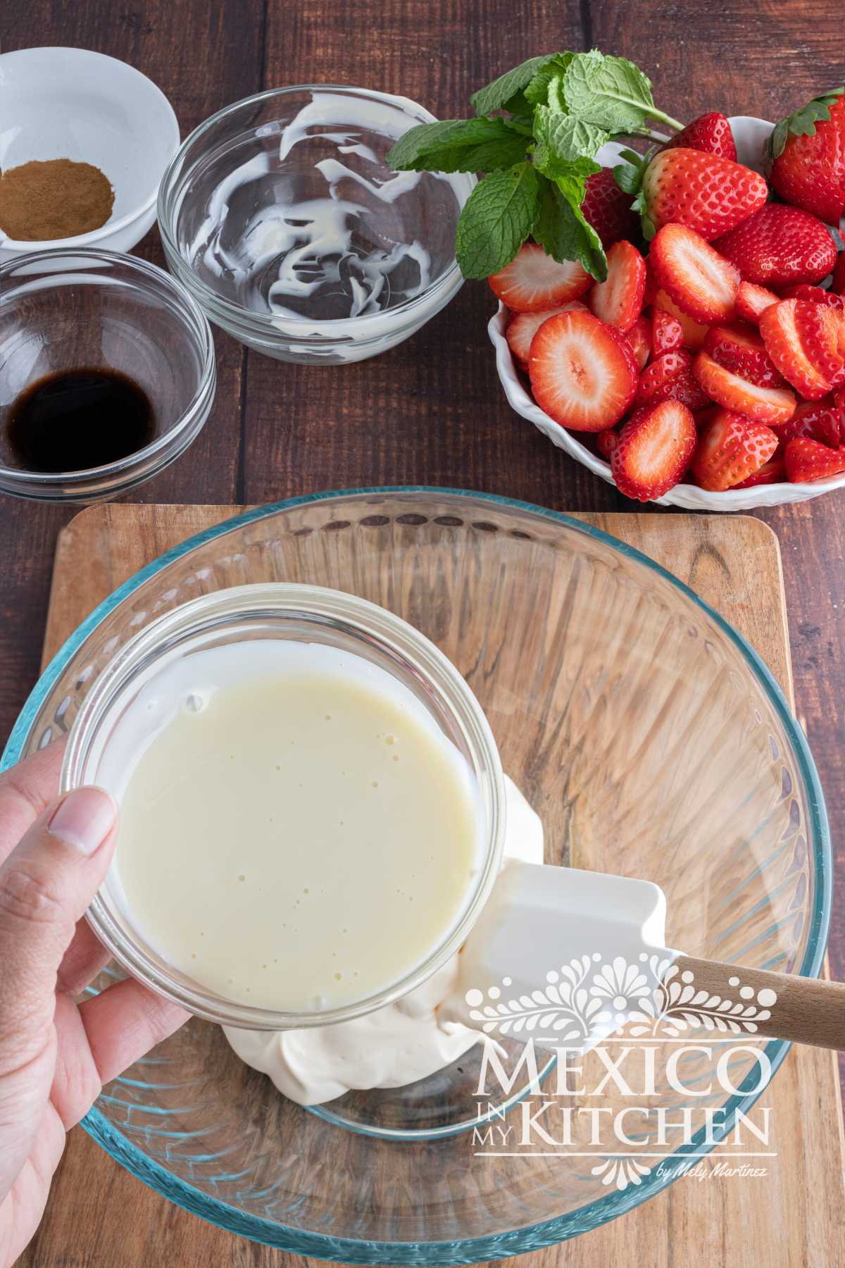 Mixing sweetened condensed milk with Mexican crema in a glass mixing bowl.