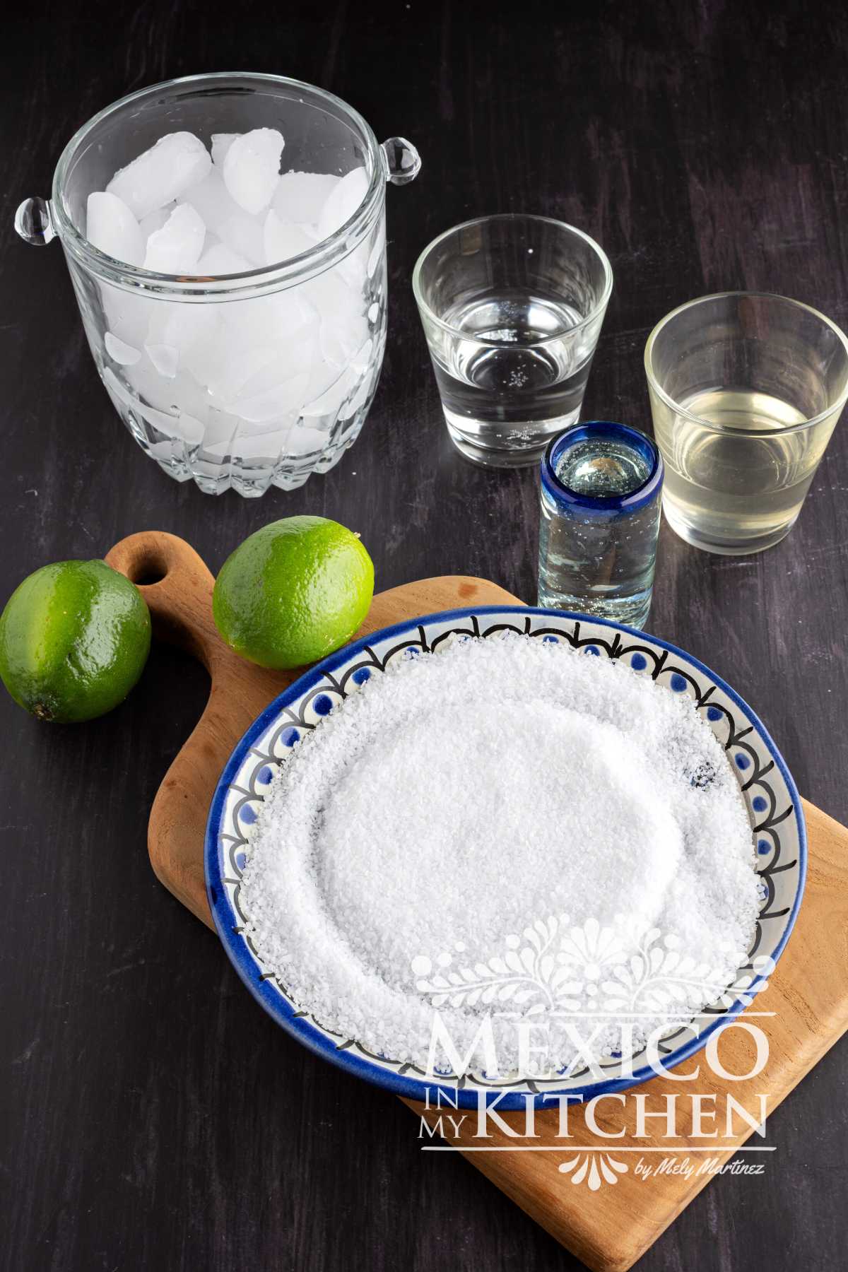 Ingredients like Ice, Tequila, Triple Sec, Simple Syrup, Lime juice and salt on displayed over a table.