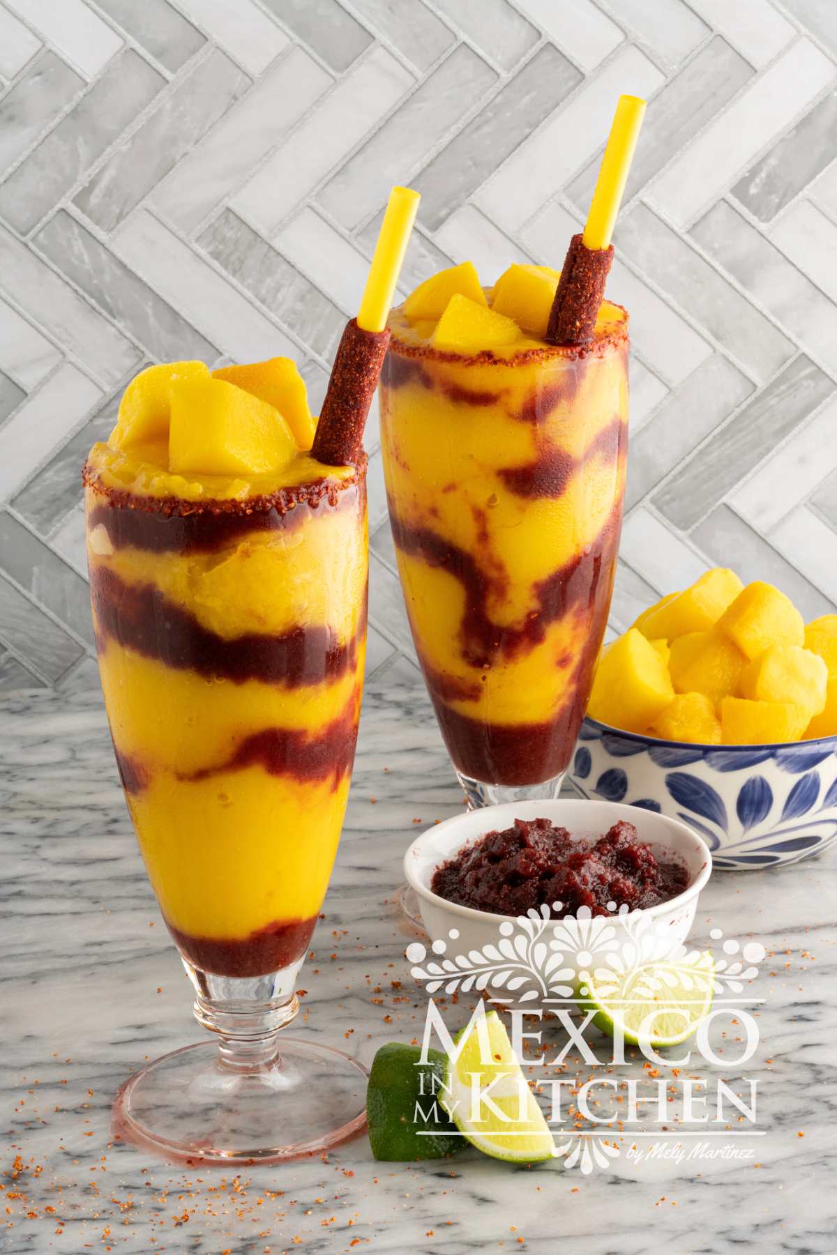 Mangonada served in a tall glass mixed with Chamoy Sauce and garnished with more mango and a tamarind stick.