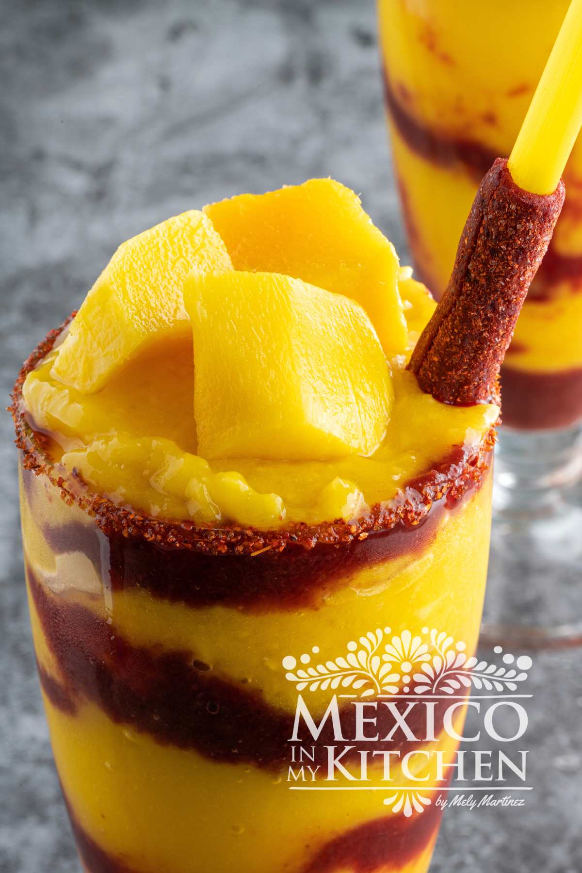 Mangonada served in a tall glass mixed with Chamoy Sauce and garnished with more mango and a tamarind stick.