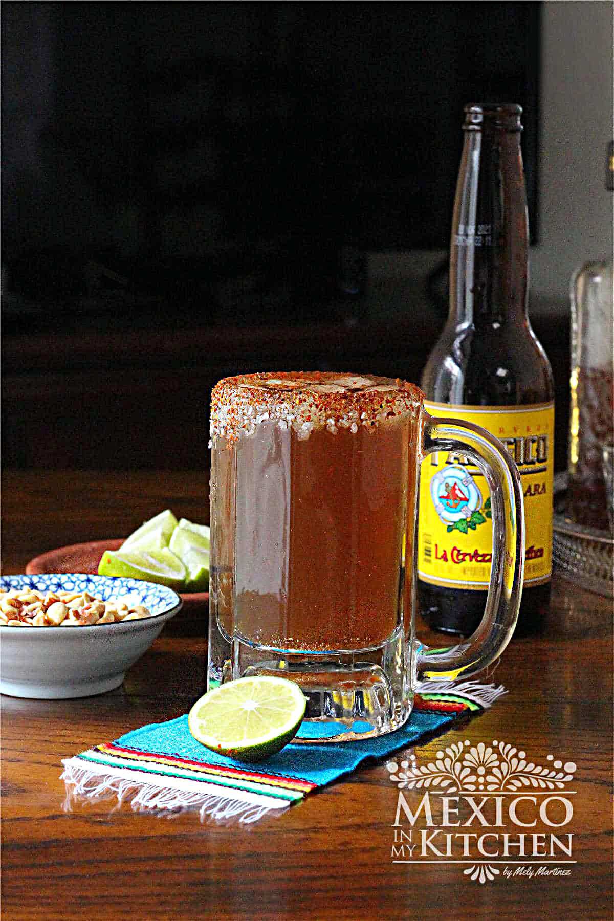 Mexican spicy beer served in a frozen glass, next to a wedge of lime and cocktail peanuts.