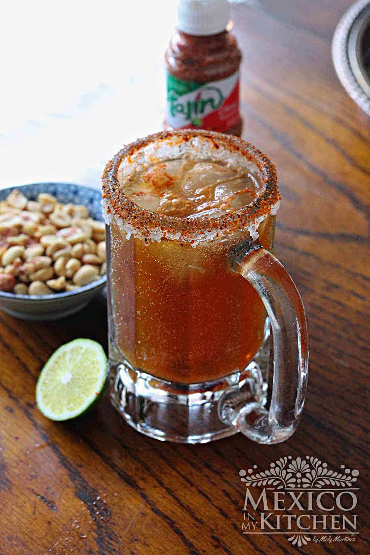 Michelada cocktail served in a frozen glass, next to a wedge of lime and cocktail peanuts.