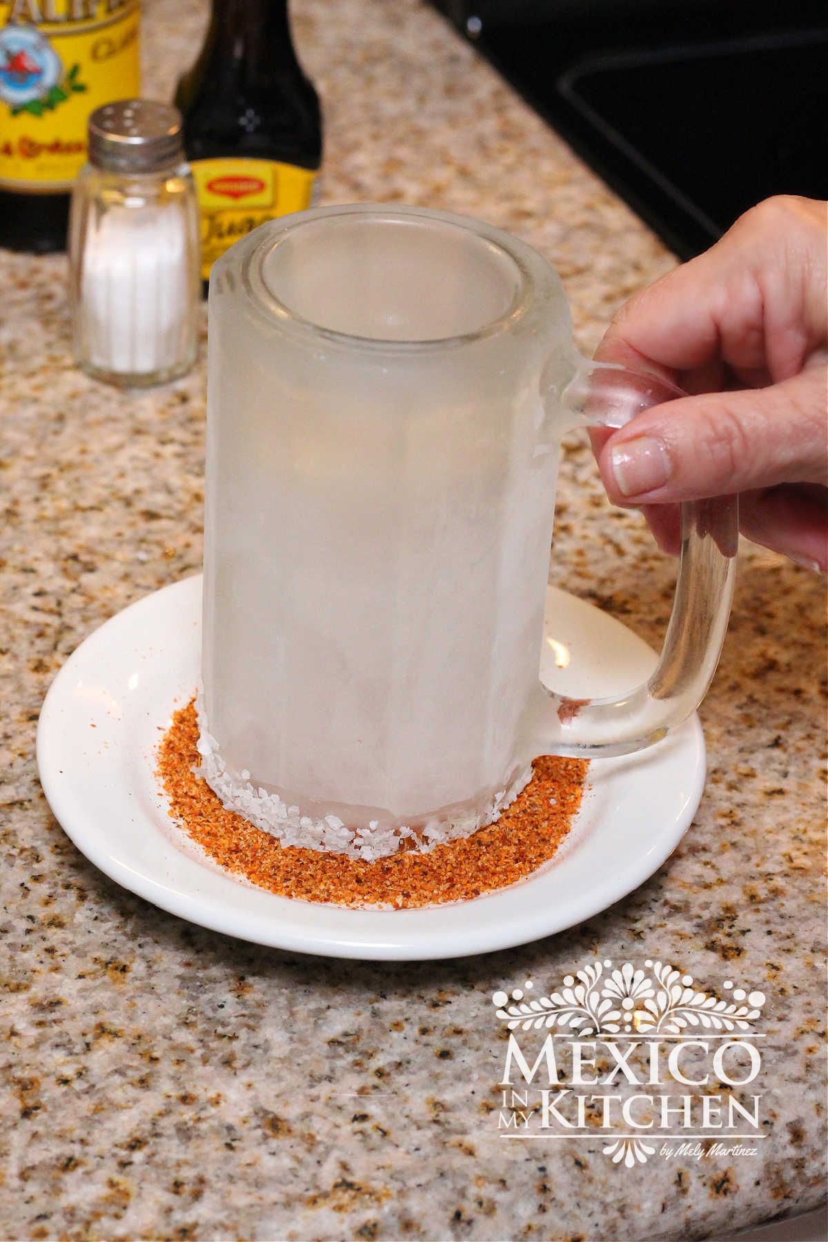Frozen glass upside down in a container of salt and tajin powder.