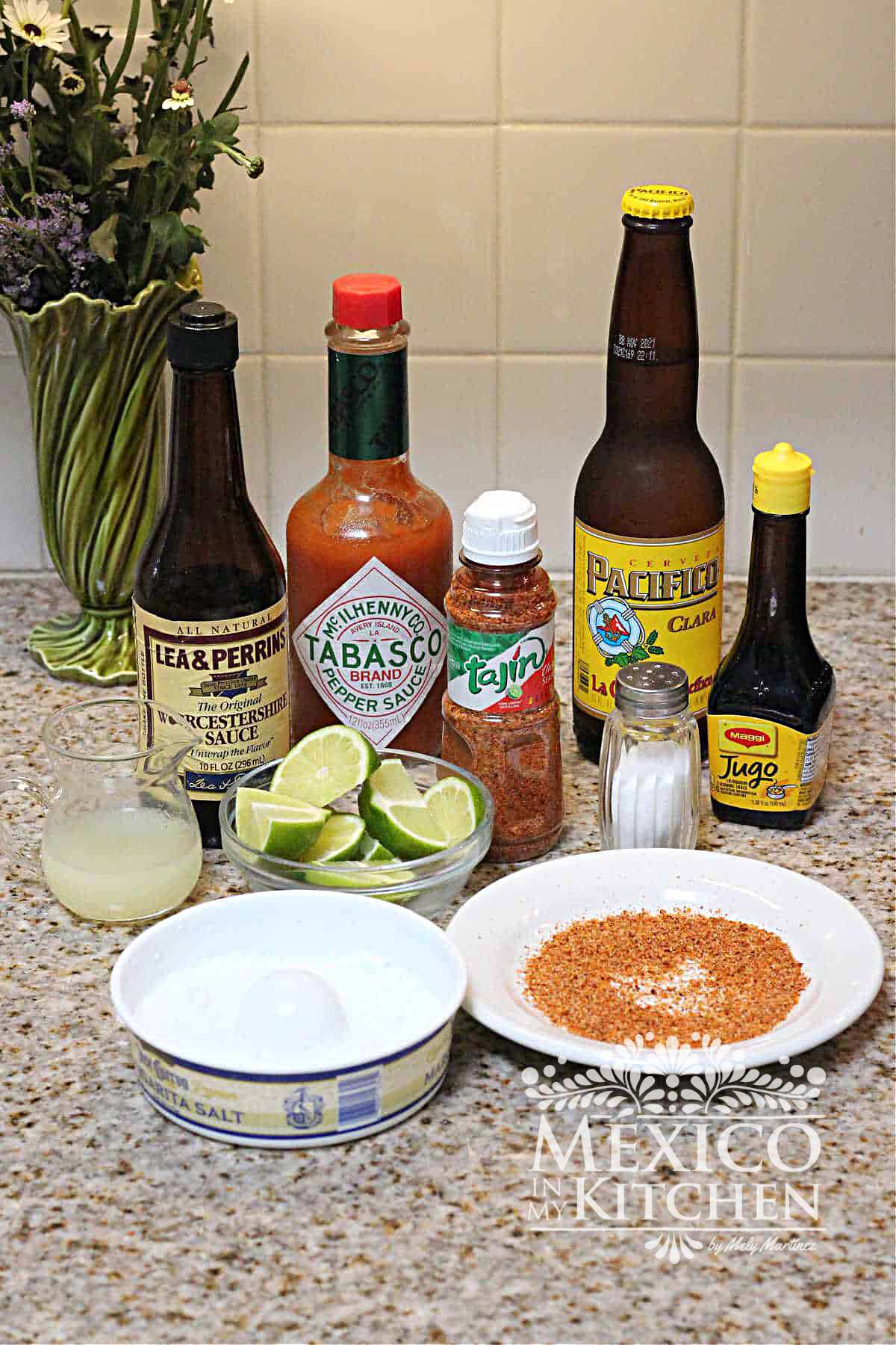 Ingredientes like beer, hot sauce, tajin powder, salt, lemons on a kitchen countertop.