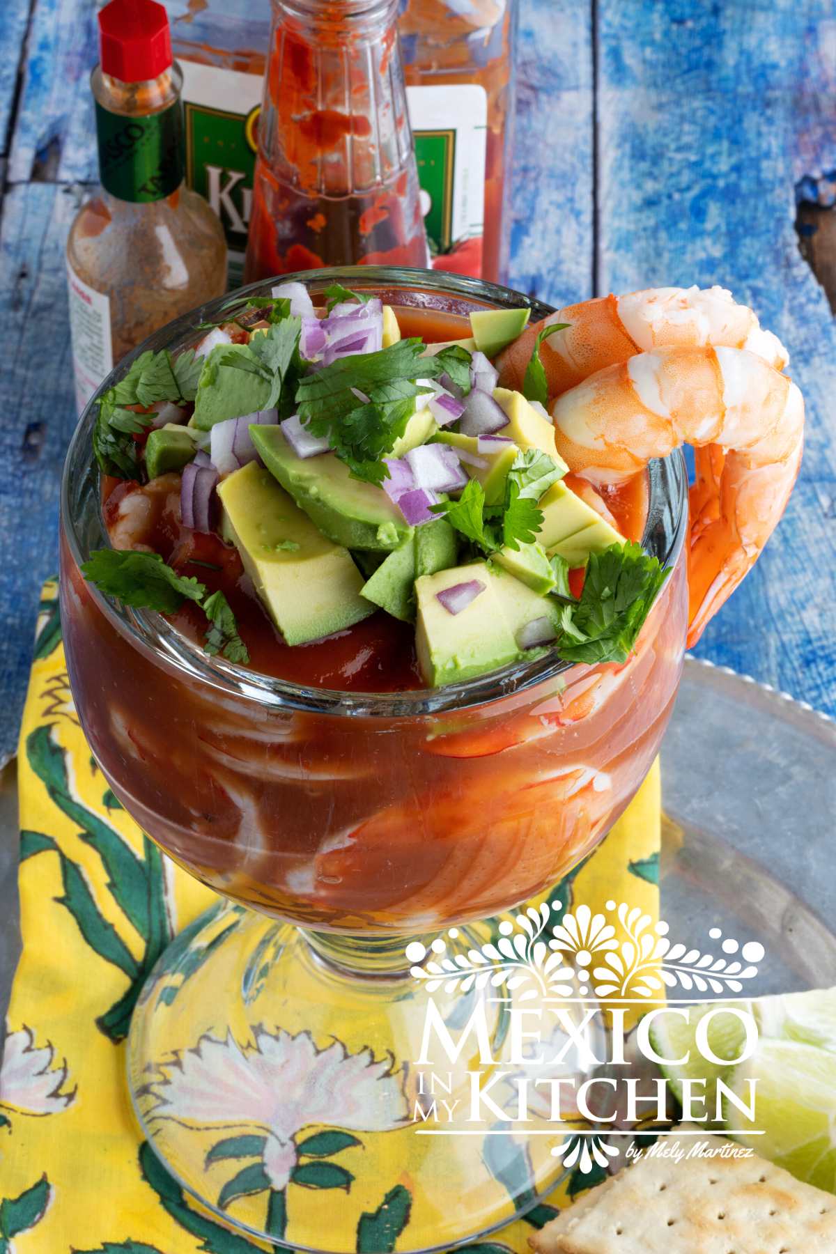 Mexican Shrimp cocktail served in a big glass bowl topped with avocado, cilantro and chopped purple onion next to saltines and lemons.