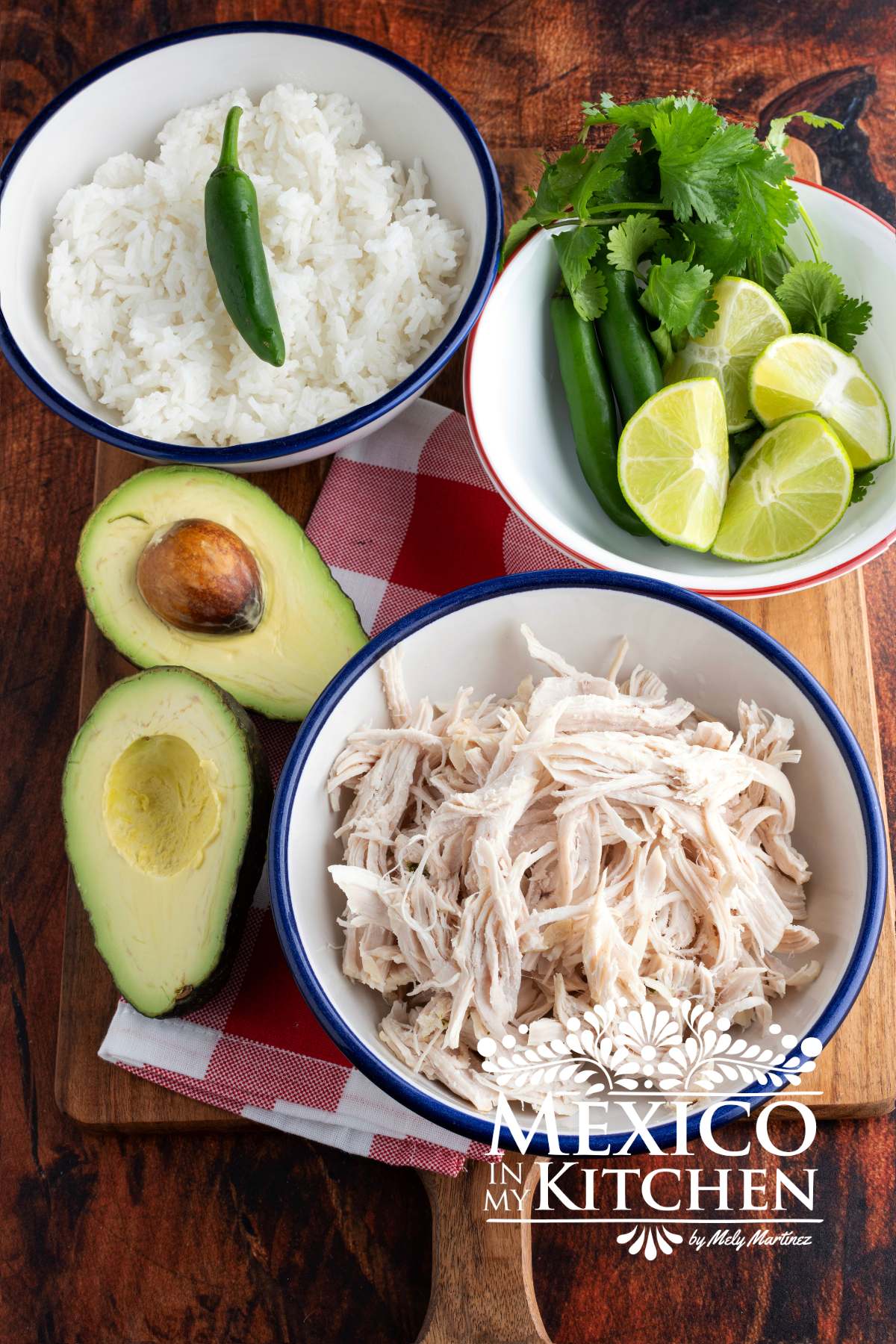 Shredded chicken served in a white bowl, next to another bowl with avocado, cilantro and limes, rices, and white rice.