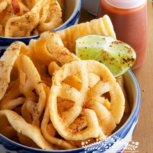 Chicharrones de harina is served in a bowl topped with chili powder and lime.