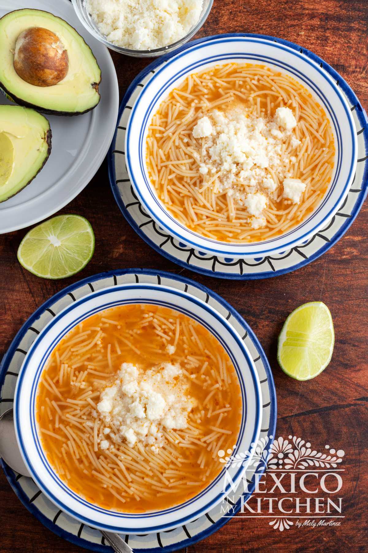 Sopa de fideo | Fideo Soup serve in white bowls, topped with queso fresco, next to avocado and lime wedges.
