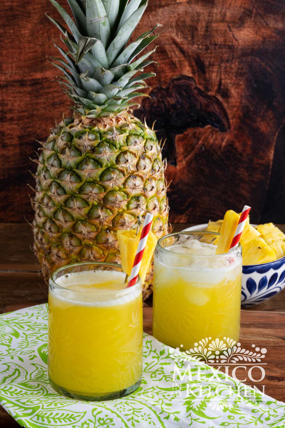 Agua de piña served in two glasses next to a pineapple and a bowl of pineapple chunks.