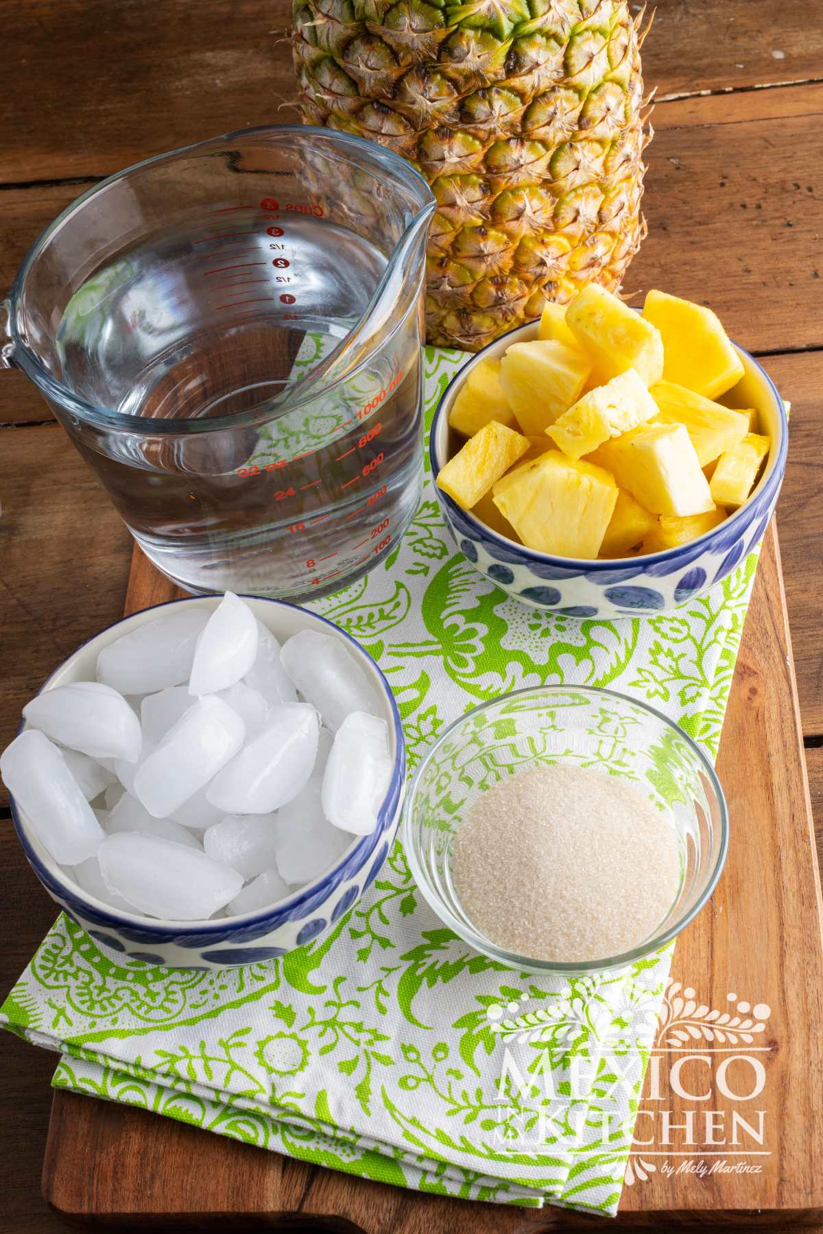 Ingredientes like ice, sugar, water and fresh pineapple, over a cutting board