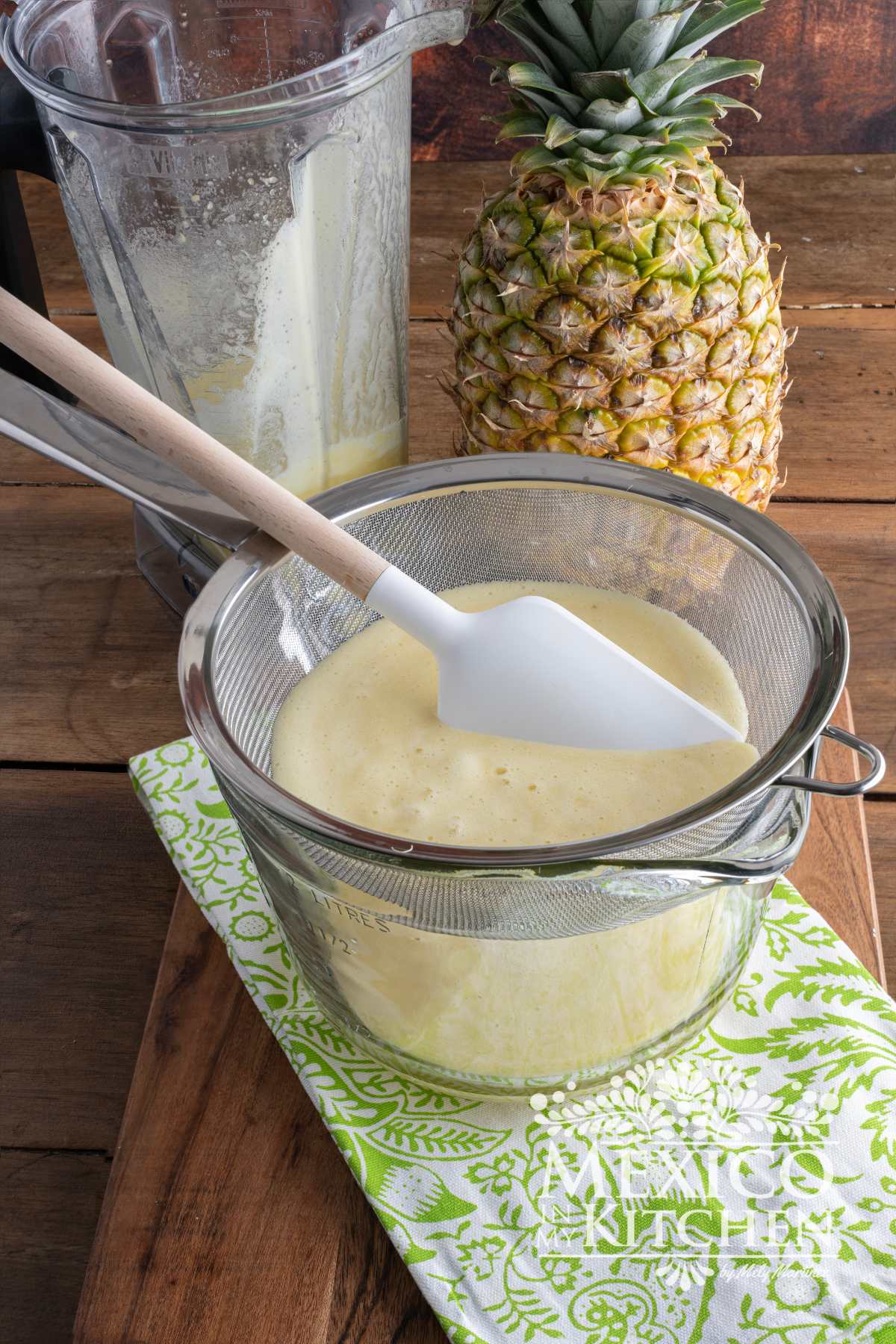 Pineapple puree in a colander over a large glass container.