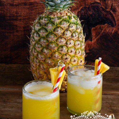 Agua de piña (pineapple agua fresca) served in glasses next to a fresh pineapple.
