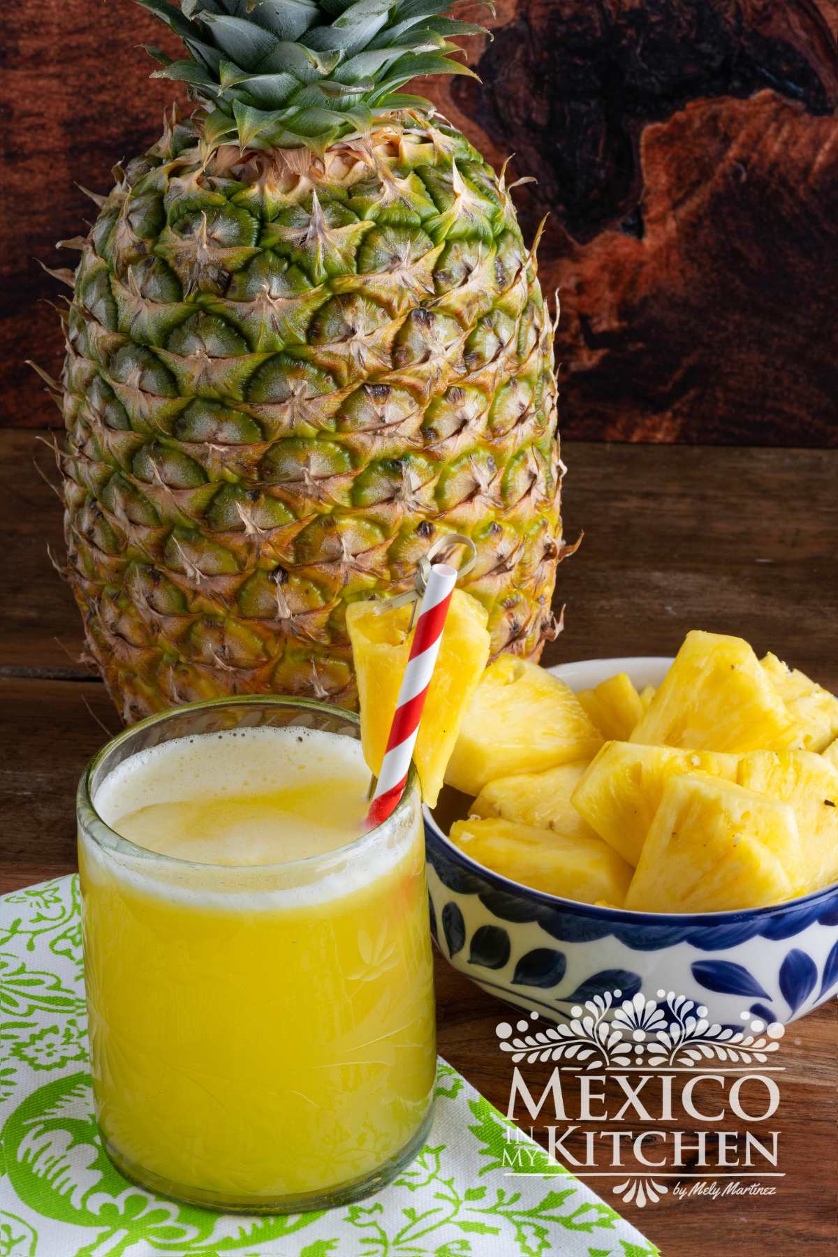 Agua de piña served in a glass next to a pineapple and a bowl of pineapple chunks.