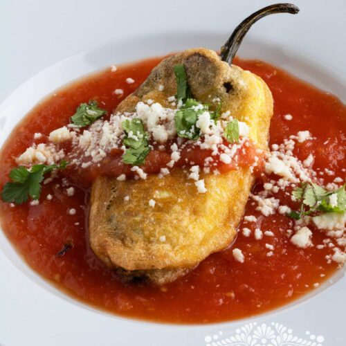 Chile relleno is served over tomato sauce and topped with queso fresco and fresh cilantro.