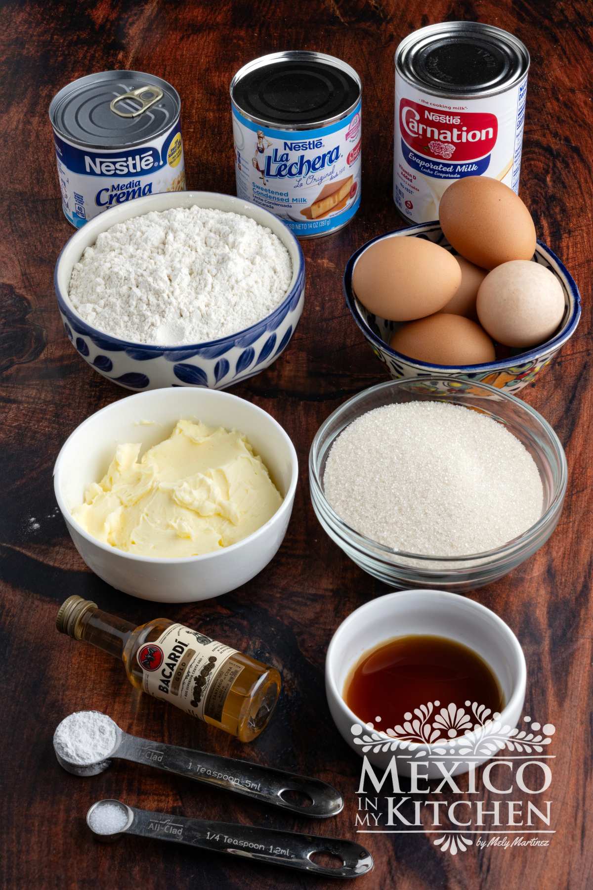Eggs, flour, sugar, butter, vanilla extract, condensed milk, evaporated milk, Media Crema milk, salt, baking powder, and rum on display.